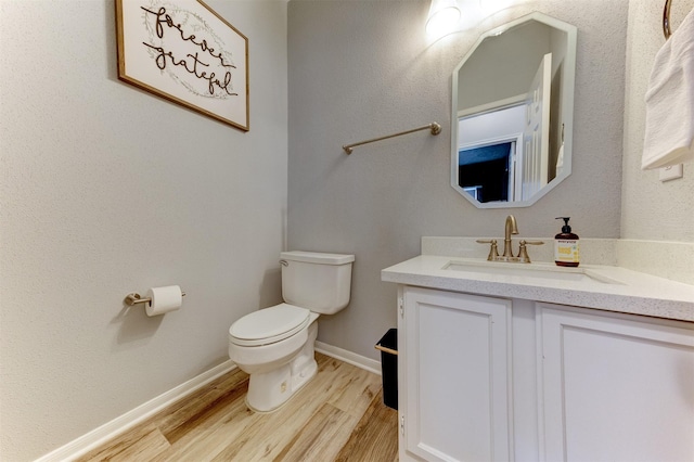 bathroom featuring baseboards, toilet, wood finished floors, and vanity