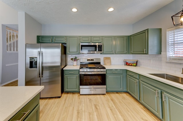 kitchen with green cabinetry, light wood-style flooring, decorative backsplash, light countertops, and appliances with stainless steel finishes