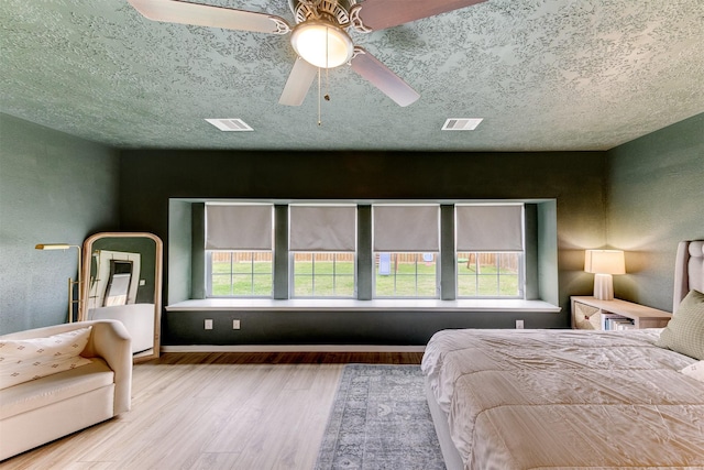 bedroom featuring baseboards, multiple windows, a textured ceiling, and wood finished floors