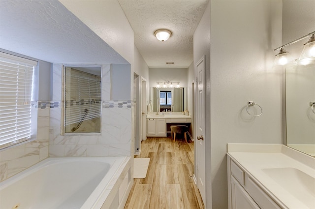 bathroom featuring two vanities, a sink, a textured ceiling, wood finished floors, and a bath