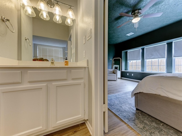 bathroom with a ceiling fan, wood finished floors, visible vents, a sink, and a textured ceiling