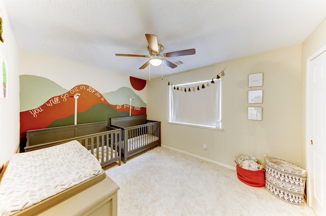 bedroom featuring ceiling fan, carpet floors, a textured ceiling, and a crib