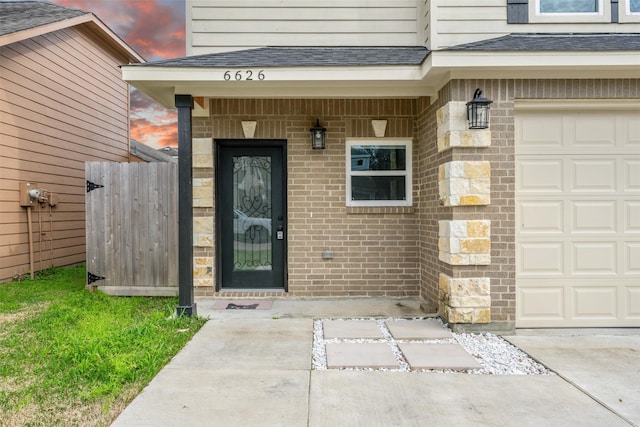 entrance to property with an attached garage, fence, brick siding, and roof with shingles