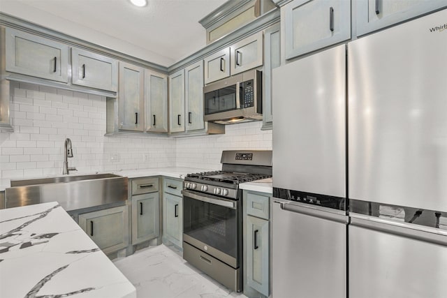 kitchen with light stone countertops, a sink, stainless steel appliances, marble finish floor, and backsplash