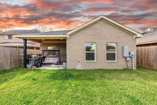 rear view of property featuring brick siding, a fenced backyard, a yard, and a patio area