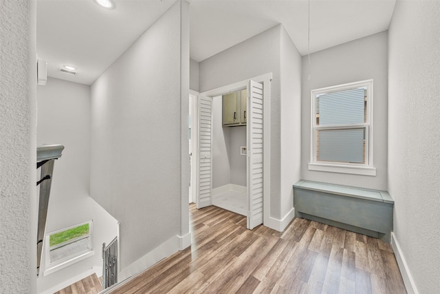 corridor featuring visible vents, wood finished floors, baseboards, and a textured wall