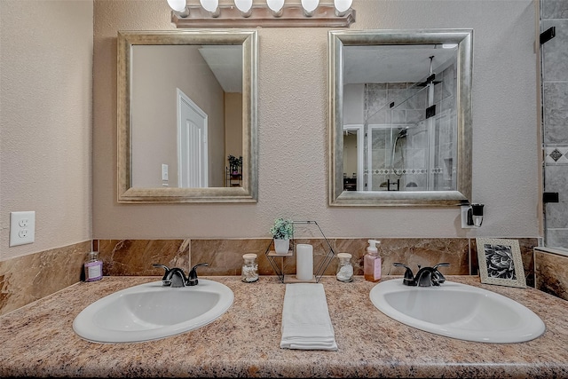 bathroom with double vanity, a shower stall, a textured wall, and a sink