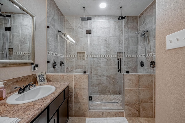 full bathroom featuring vanity, a shower stall, a textured wall, and a textured ceiling