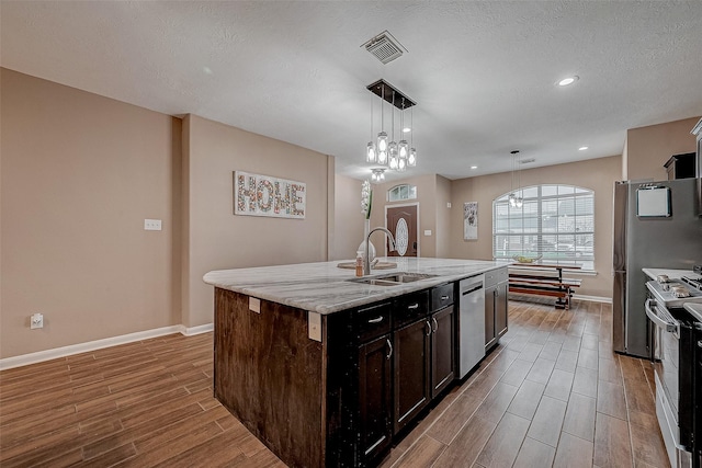 kitchen with visible vents, wood finish floors, a kitchen island with sink, a sink, and appliances with stainless steel finishes