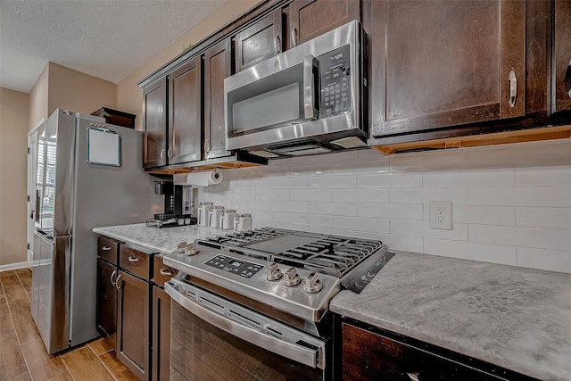 kitchen featuring wood finish floors, a textured ceiling, stainless steel appliances, dark brown cabinetry, and decorative backsplash