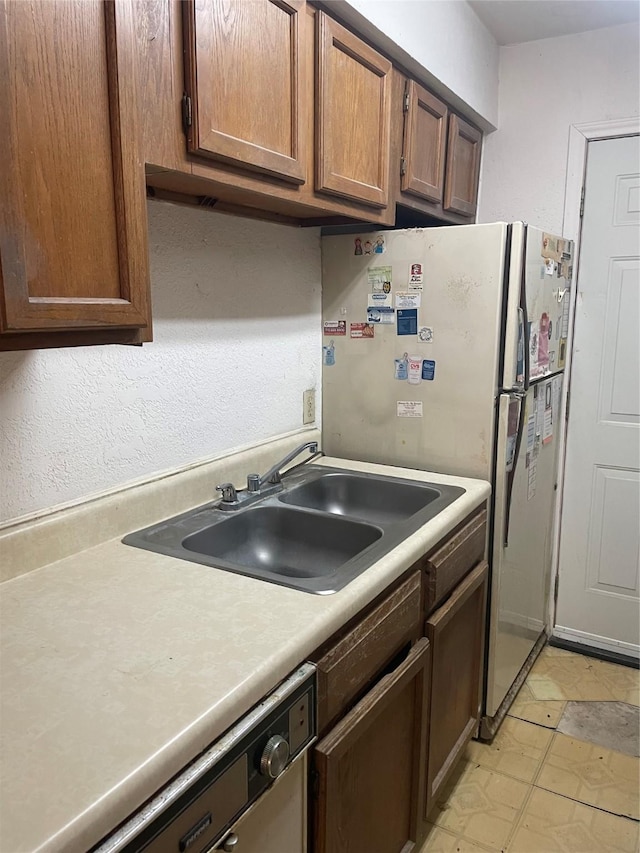 kitchen with light countertops, dishwashing machine, brown cabinets, freestanding refrigerator, and a sink