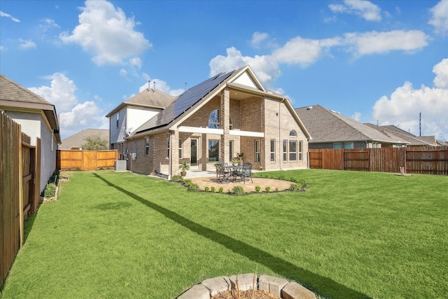 rear view of property with brick siding, roof mounted solar panels, a lawn, a fenced backyard, and a patio area