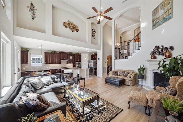 living room with ceiling fan, stairway, light wood-type flooring, a fireplace, and arched walkways