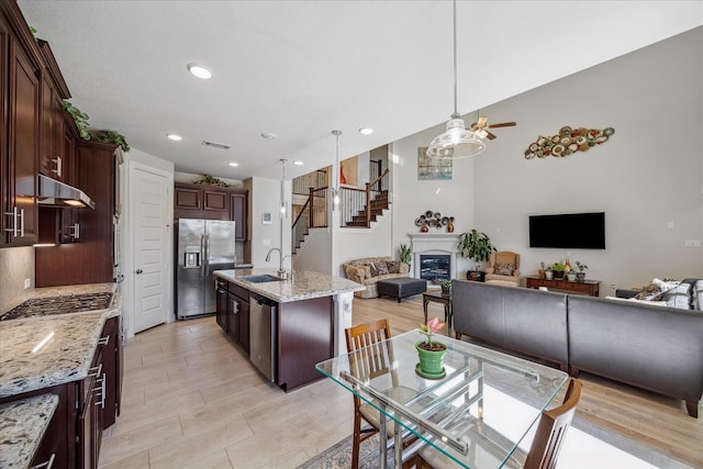 kitchen featuring visible vents, a sink, open floor plan, a glass covered fireplace, and appliances with stainless steel finishes