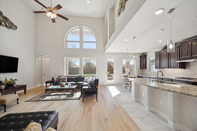 living room with a ceiling fan, visible vents, baseboards, light wood-style flooring, and arched walkways