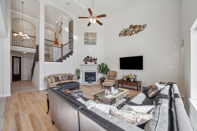 living area with visible vents, stairway, light wood-style flooring, a towering ceiling, and a glass covered fireplace