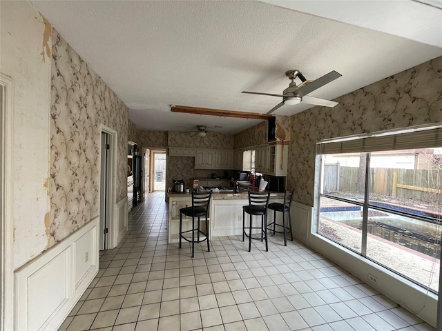 kitchen with wallpapered walls, a peninsula, wainscoting, a textured ceiling, and a kitchen breakfast bar