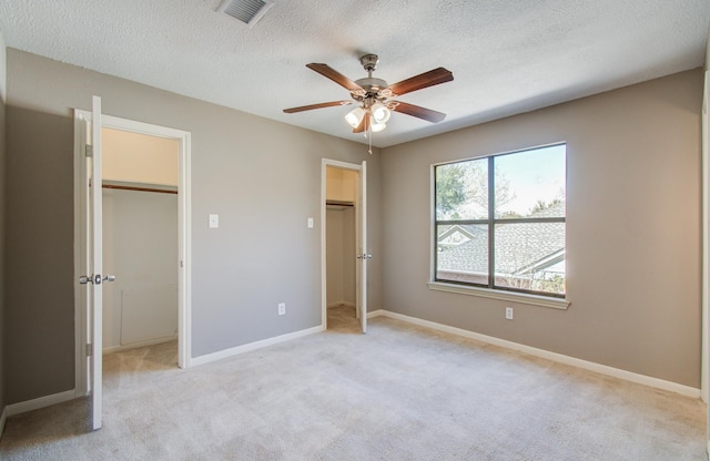 unfurnished bedroom featuring light carpet, visible vents, a walk in closet, and baseboards