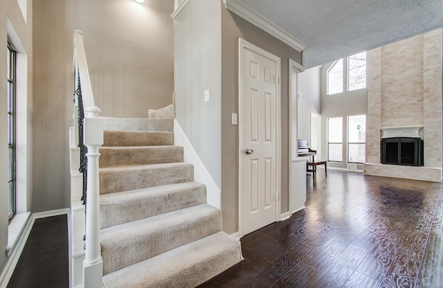 staircase featuring wood finished floors, baseboards, a fireplace with raised hearth, ornamental molding, and a textured ceiling