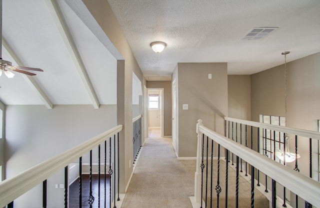 hallway with visible vents, an upstairs landing, light carpet, a textured ceiling, and baseboards