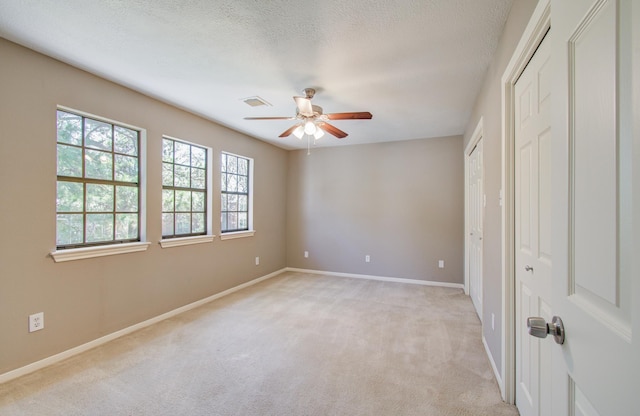 unfurnished bedroom featuring visible vents, light carpet, a textured ceiling, and multiple closets