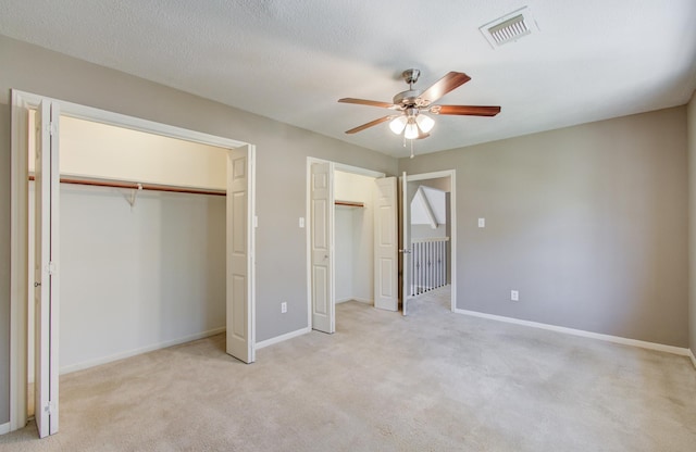 unfurnished bedroom featuring multiple closets, light colored carpet, visible vents, and baseboards