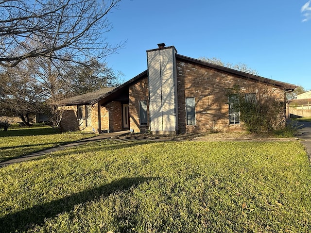 exterior space featuring a yard, brick siding, and a chimney