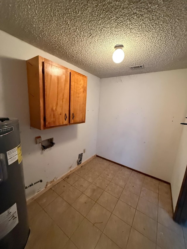 clothes washing area with visible vents, electric water heater, a textured ceiling, cabinet space, and baseboards