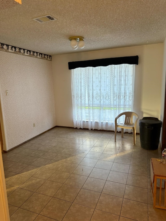 spare room featuring wallpapered walls, light tile patterned floors, visible vents, and a textured ceiling