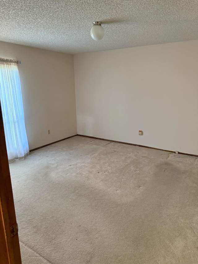 spare room with a textured ceiling, baseboards, and light carpet