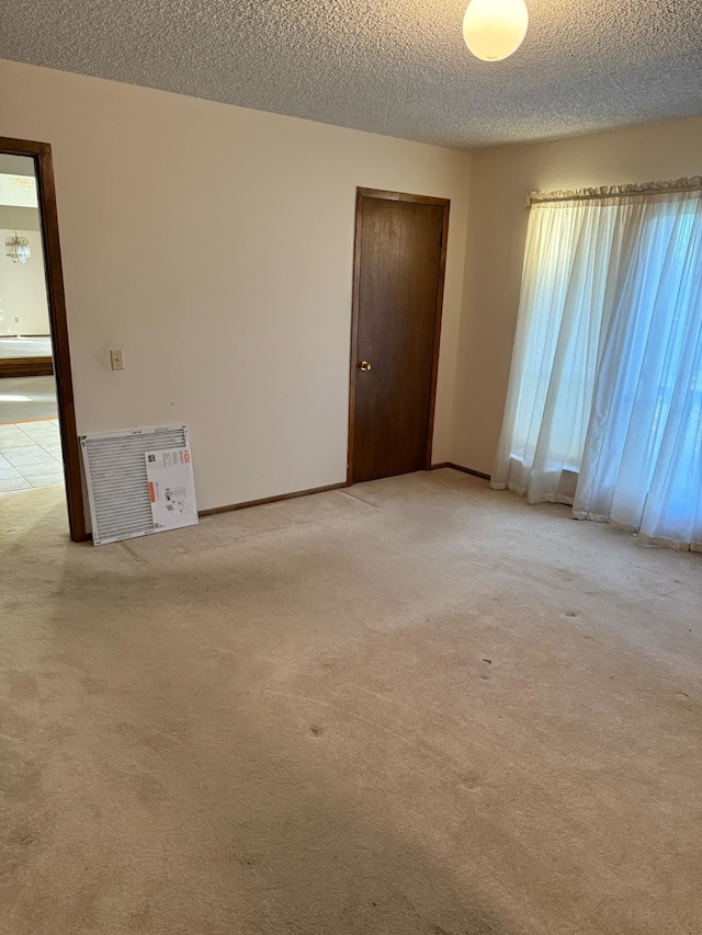 spare room featuring baseboards, light colored carpet, and a textured ceiling