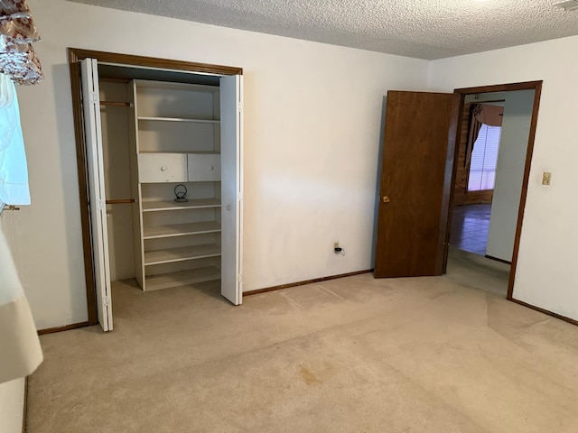 unfurnished bedroom featuring baseboards, light carpet, a textured ceiling, and a closet