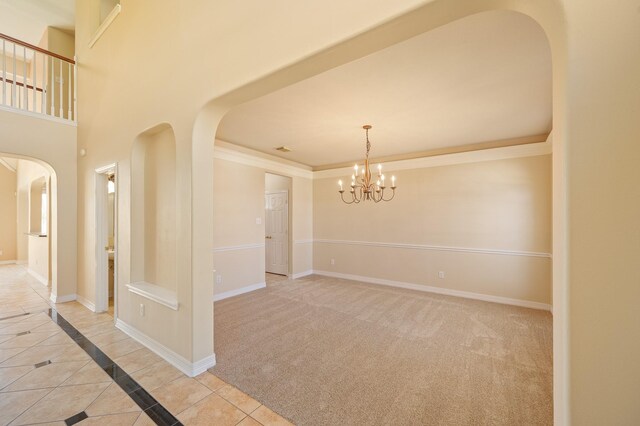 spare room featuring light carpet, arched walkways, crown molding, baseboards, and a chandelier