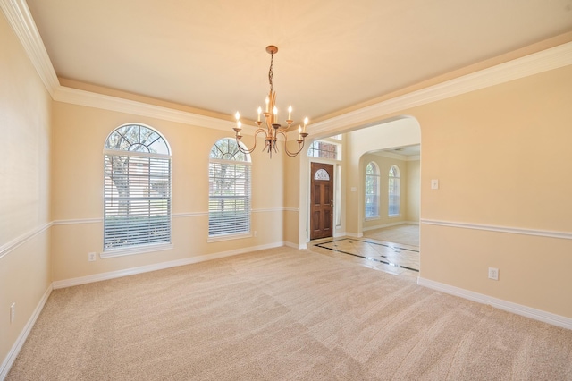 carpeted empty room featuring a notable chandelier, baseboards, arched walkways, and ornamental molding