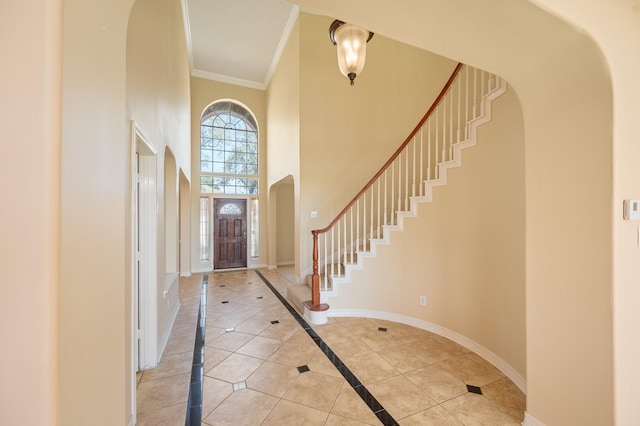 foyer with ornamental molding, arched walkways, light tile patterned floors, baseboards, and a towering ceiling