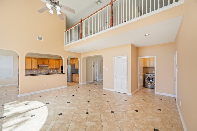 living area featuring washer / clothes dryer, baseboards, arched walkways, and ceiling fan