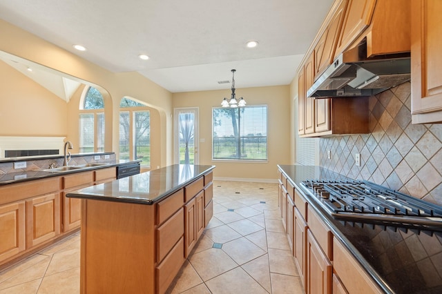 kitchen with a notable chandelier, a sink, under cabinet range hood, backsplash, and a center island