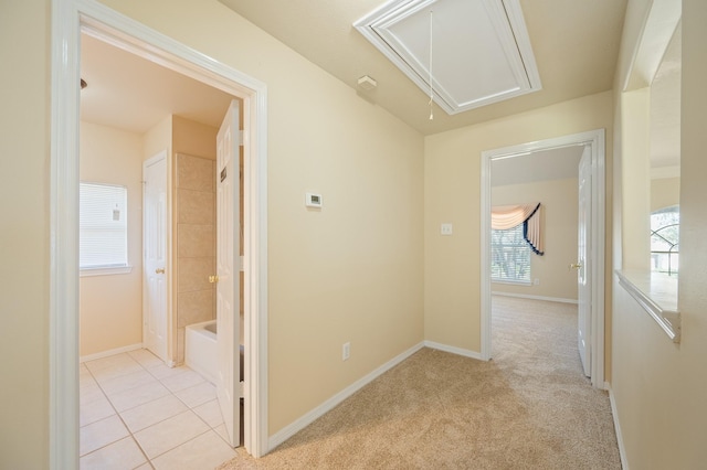 hall with light tile patterned flooring, light colored carpet, attic access, and baseboards