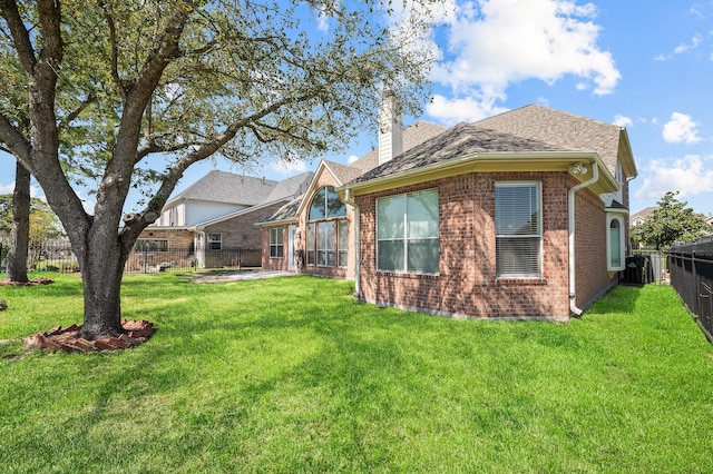 back of property featuring a yard, a shingled roof, a chimney, fence private yard, and brick siding