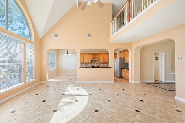 unfurnished living room with ceiling fan with notable chandelier, light tile patterned floors, visible vents, and baseboards