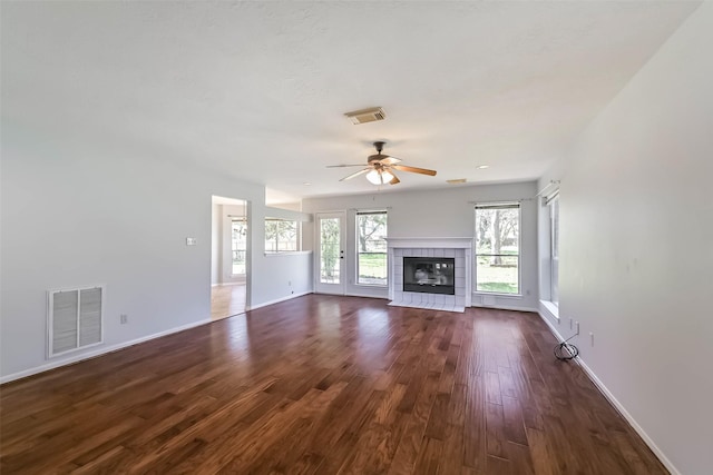 unfurnished living room featuring a tiled fireplace, dark wood-style floors, visible vents, and baseboards