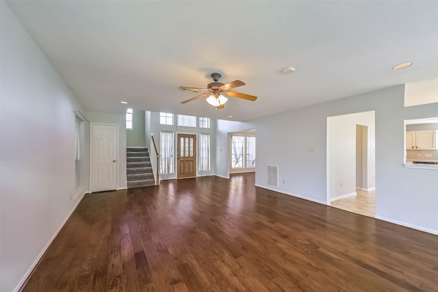 unfurnished living room with a ceiling fan, wood finished floors, visible vents, baseboards, and stairs