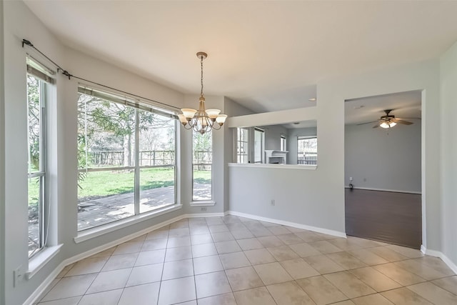 unfurnished dining area featuring light tile patterned floors, a healthy amount of sunlight, ceiling fan with notable chandelier, and baseboards