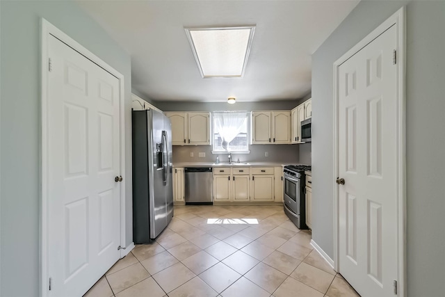 kitchen featuring light tile patterned floors, stainless steel appliances, cream cabinetry, and a sink