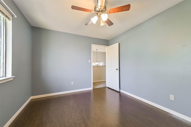 unfurnished room with dark wood-style floors, ceiling fan, a wealth of natural light, and baseboards