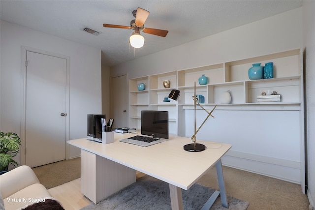 office featuring visible vents, light carpet, a textured ceiling, and ceiling fan