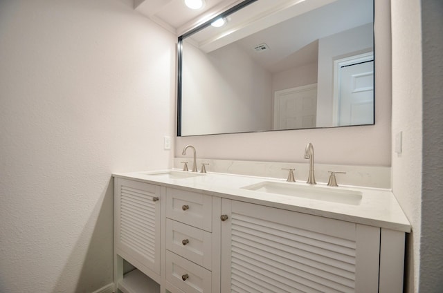 bathroom featuring double vanity, visible vents, a textured wall, and a sink