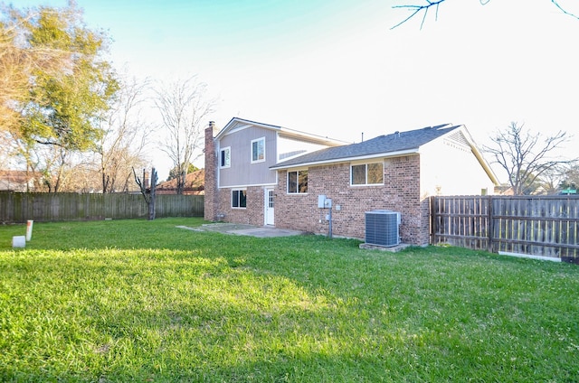 rear view of house with central AC, a fenced backyard, a yard, brick siding, and a chimney