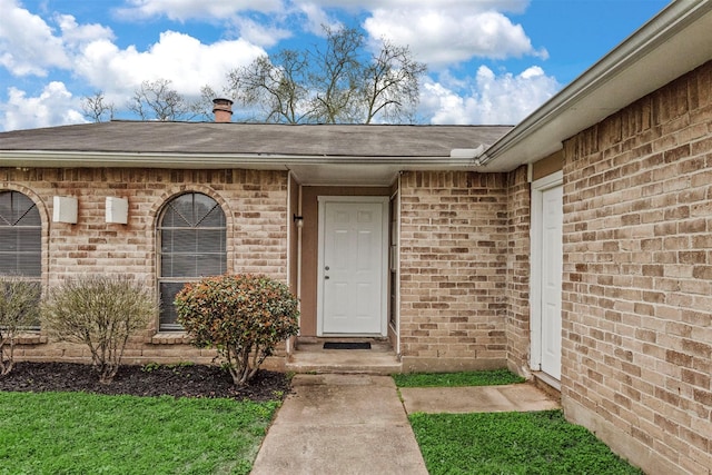 doorway to property featuring brick siding and roof with shingles