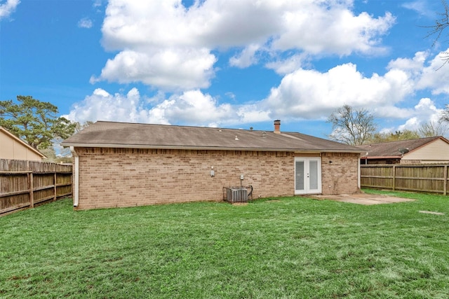 rear view of property with brick siding, a fenced backyard, a lawn, and a patio area